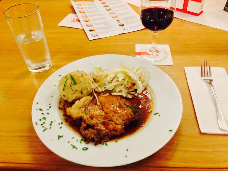 Pork roast with a giant dumpling and coleslaw, topped off with red wine.